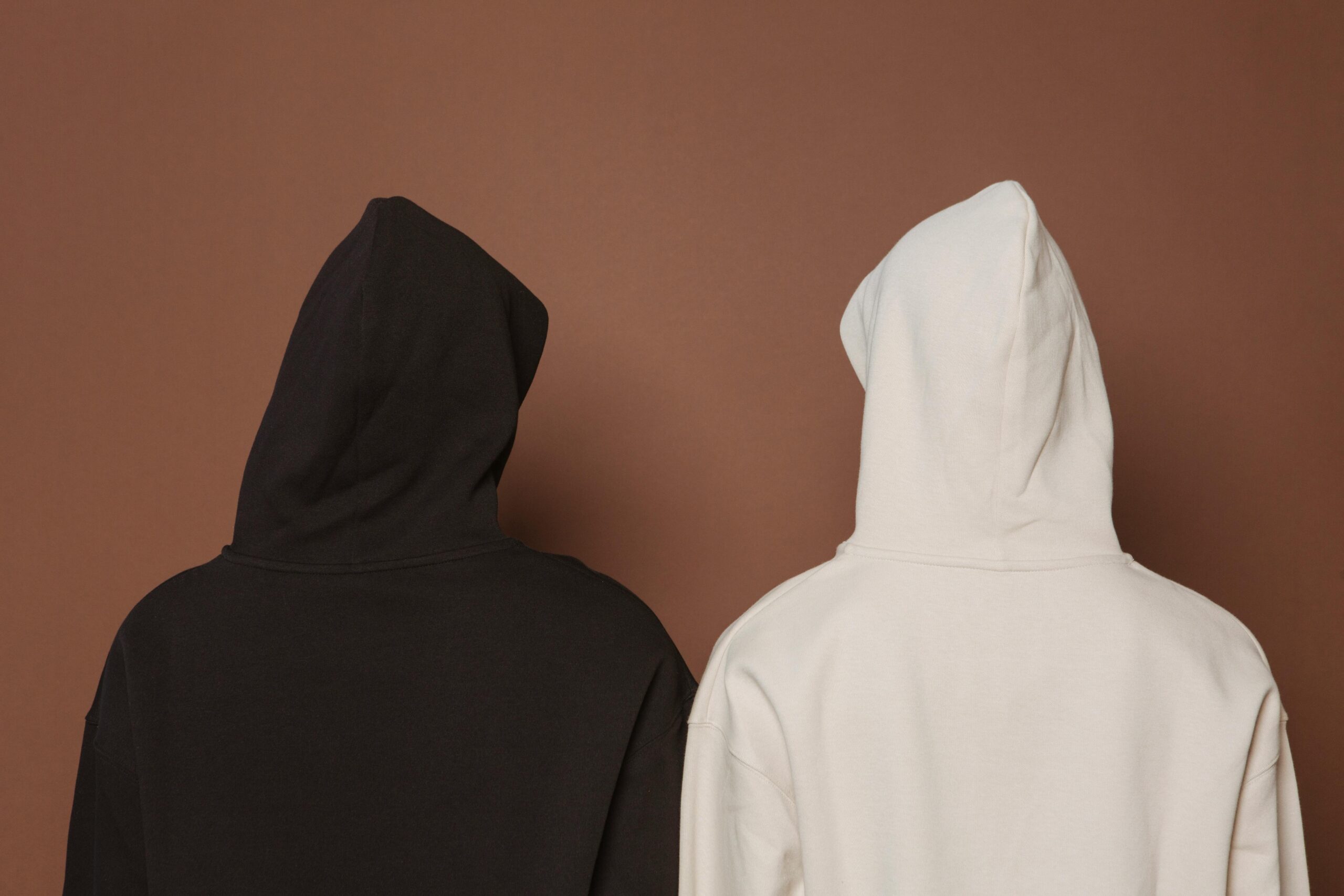 pexels photo 7479825 7479825 Back view of two hoodies in white and black against a brown background.