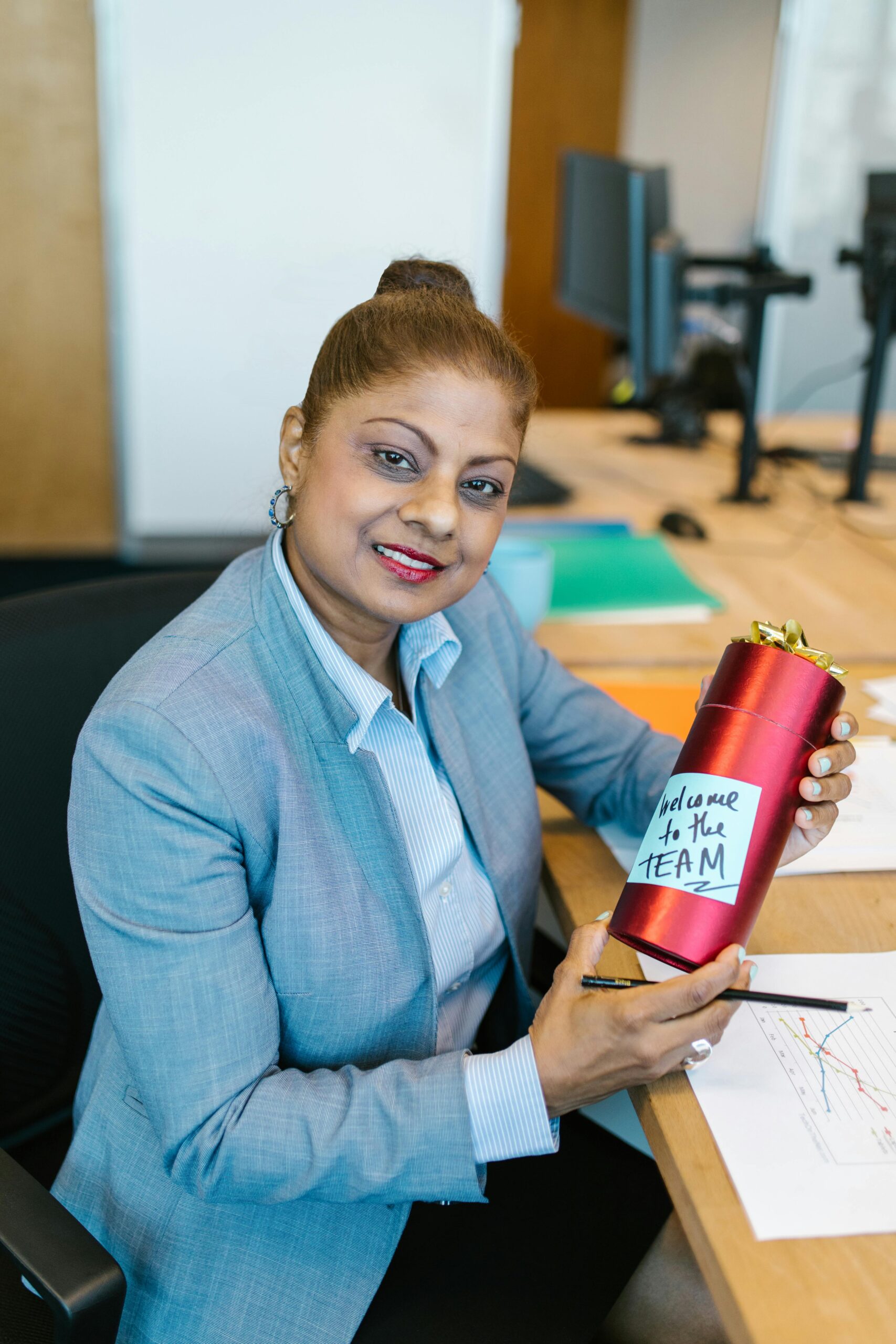Smiling businesswoman receiving a welcome gift in an office setting, holding a pen.